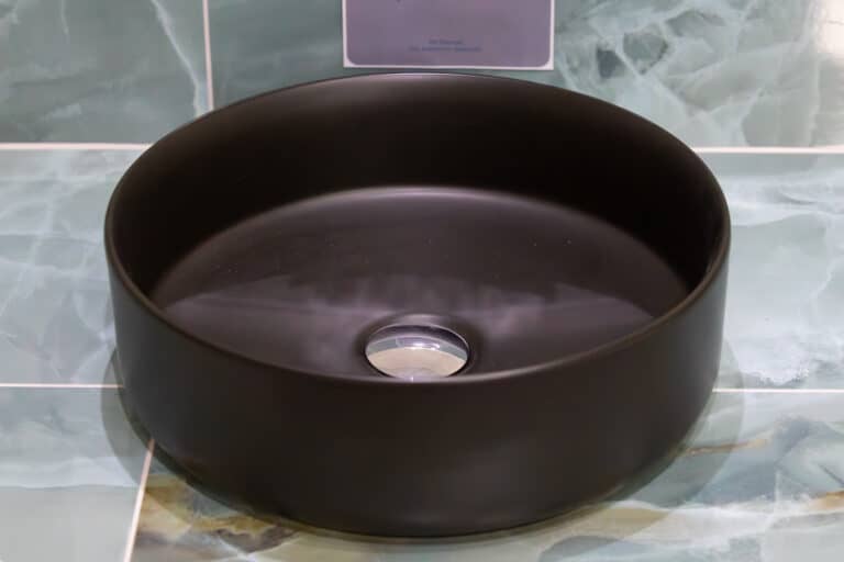 A dark bronze countertop basin on a green marble effect tiled surface