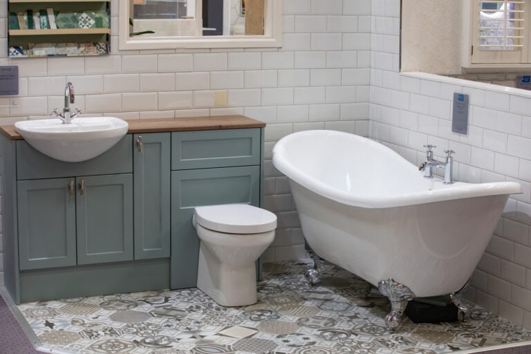 A grey vanity unit and WC beside a roll top bath on a patterned floor
