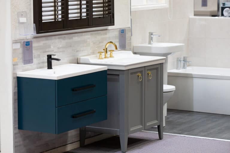 A teal vanity unit with a brass tap, beside a grey traditional vanity and a bath