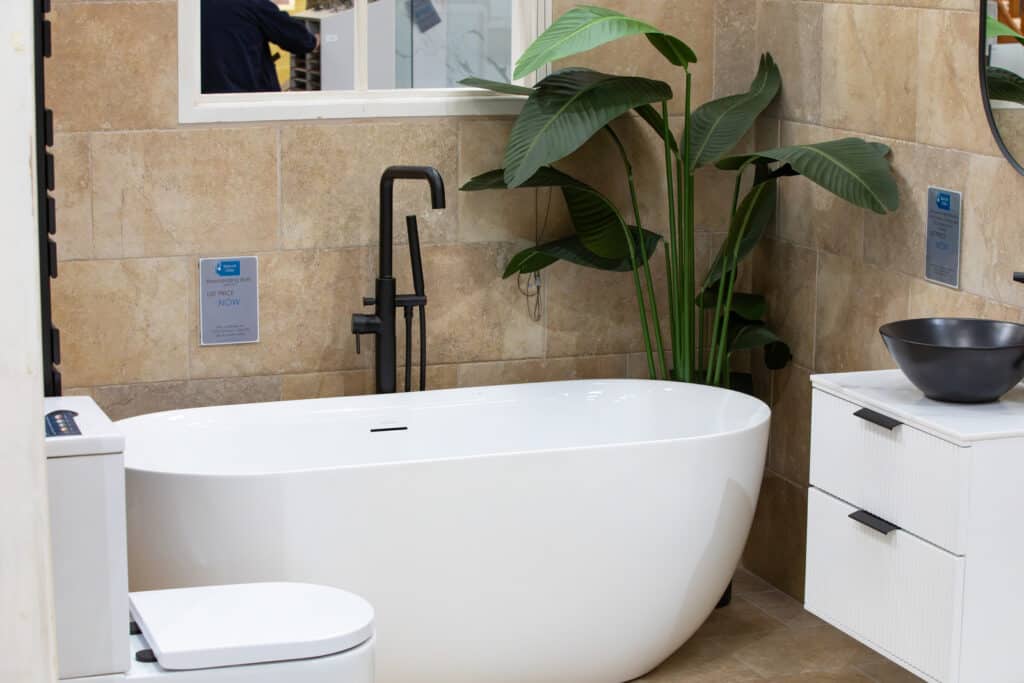 A white freestanding bath with a black tap and a large leafy plant behind