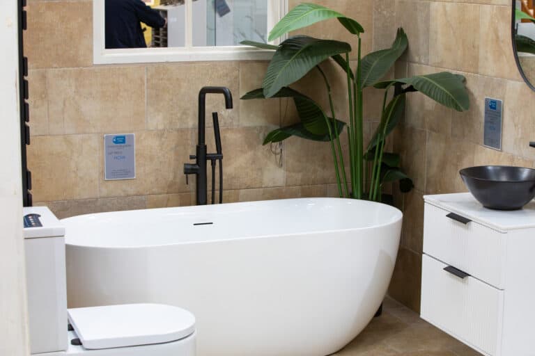 A white freestanding bath with a black tap and a large leafy plant behind