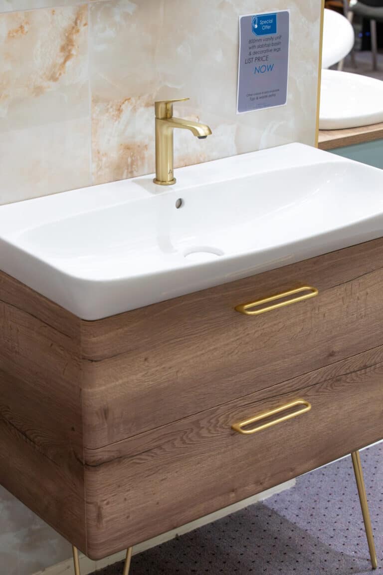 A white basin on a wood vanity unit with a brass tap and brass legs