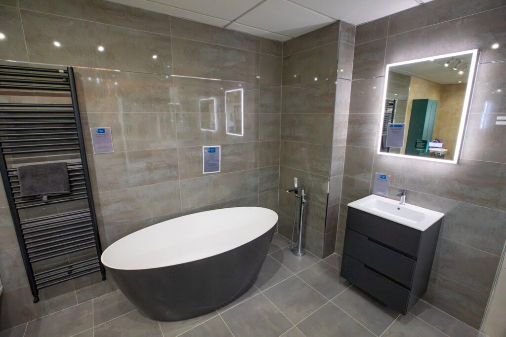 A grey freestanding bath beside a tall black towel radiator