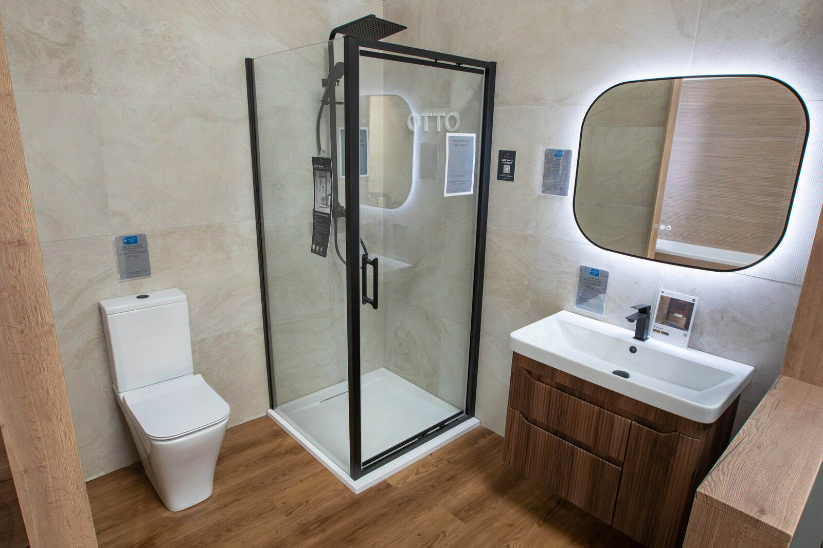 A black framed shower enclosure with a WC, wood vanity unit and rounded mirror