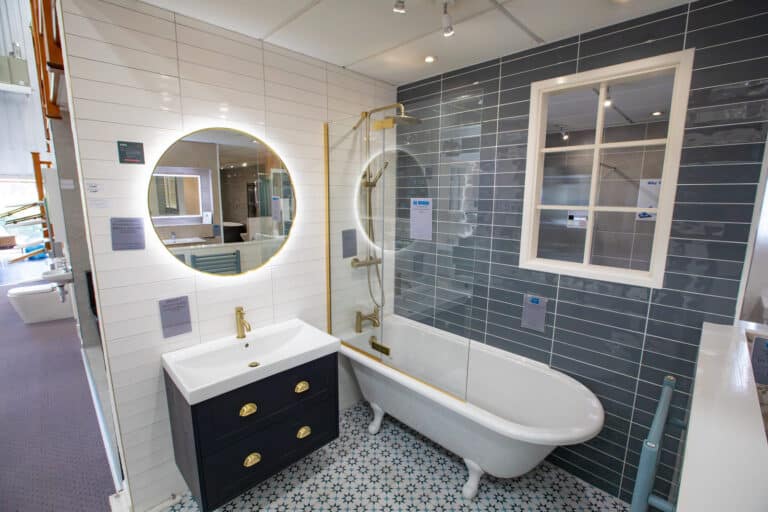 A roll top bath with a navy vanity unit, brass taps and a patterned floor