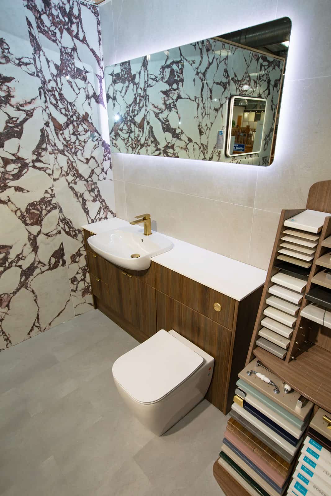 A bath and WC against a claret marble effect tiled wall, beside tile samples