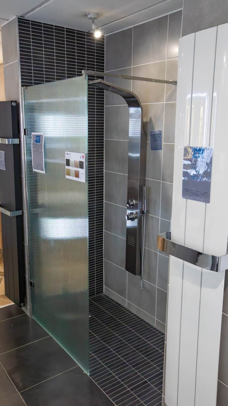 A walk in shower with dark tiling and a glass screen