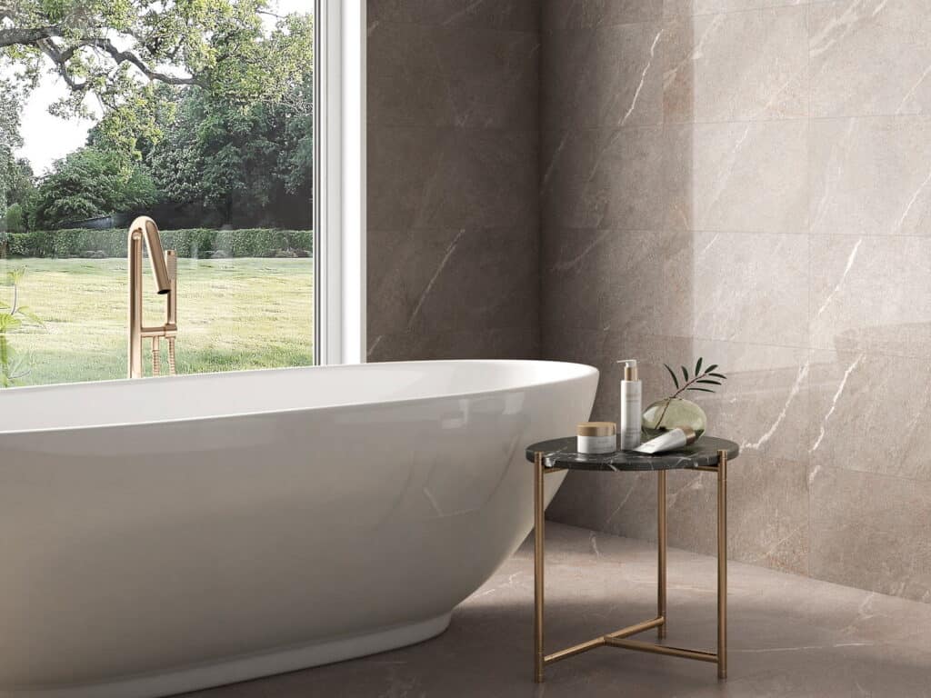 Taupe marble-effect wall and floor tiles in a bathroom with a freestanding bath