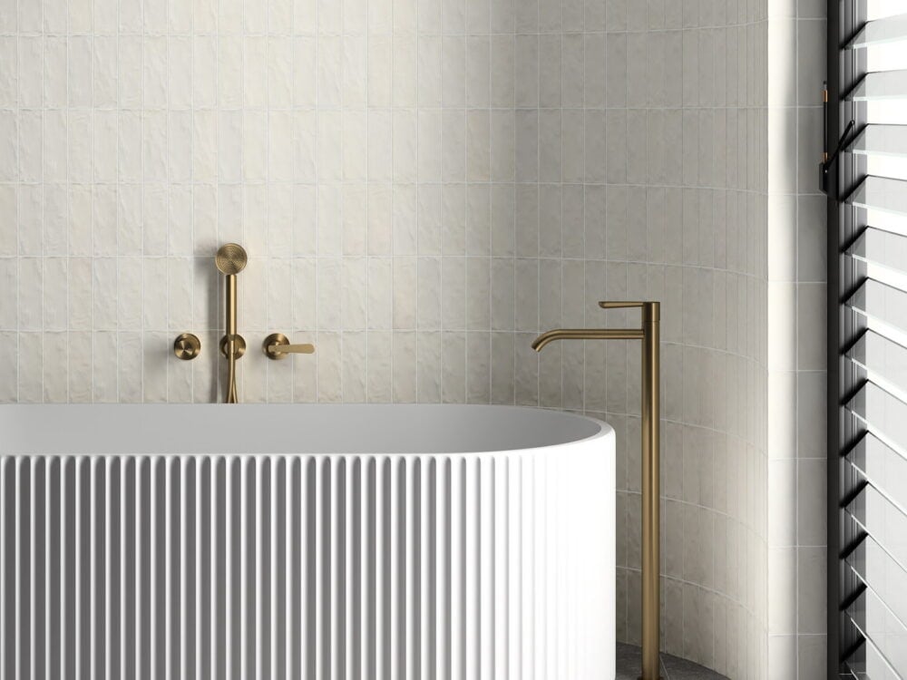 Craven Dunnill Sabbia Silica White square wall tiles beside a fluted freestanding bath with brushed gold taps