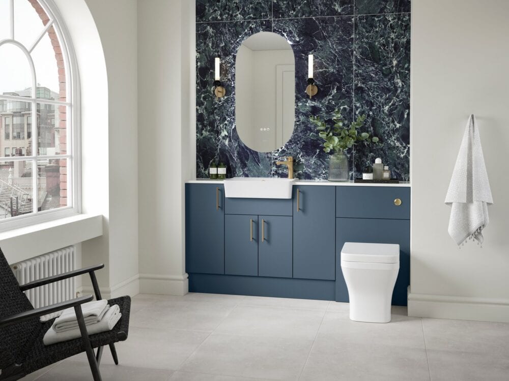 Veldeau Aston muted blue fitted furniture with an illuminated mirror and dark marble wall