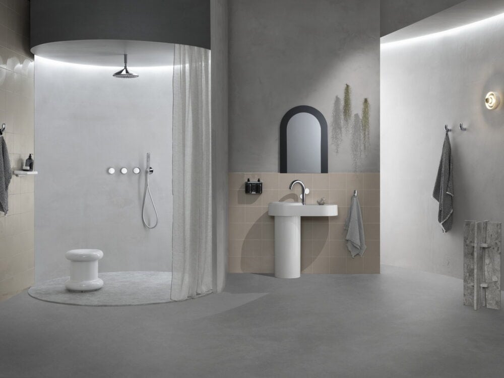 VitrA curved walk-in shower with a pedestal washbasin and arched mirror in a pale bathroom