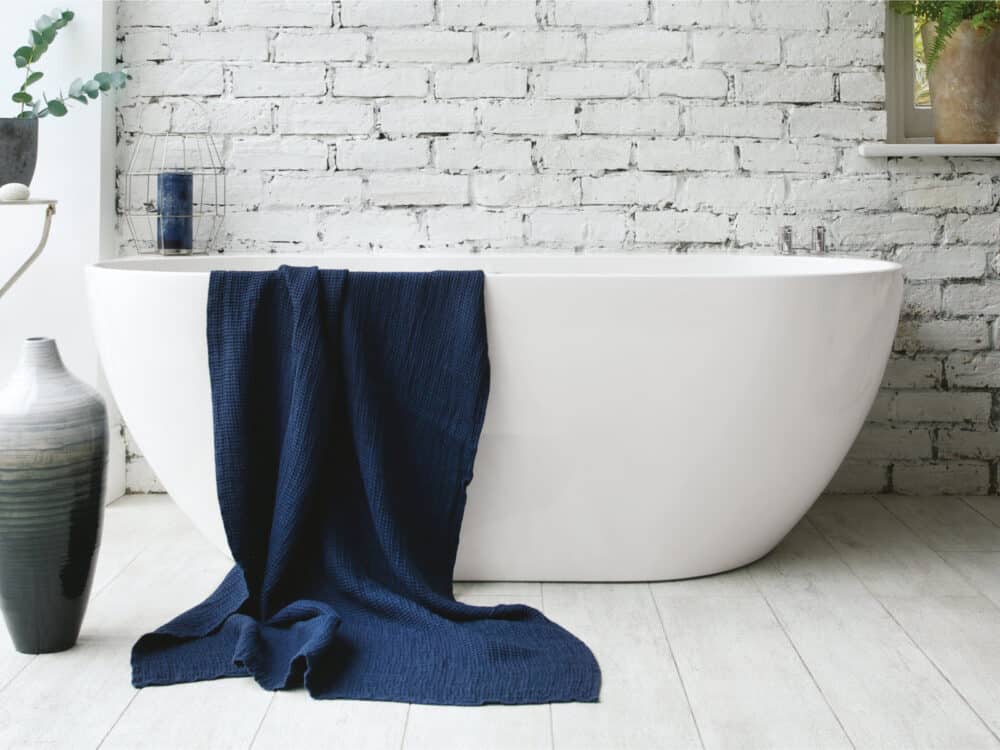 Waters Loche freestanding bath against white-painted brick with a navy towel over the rim