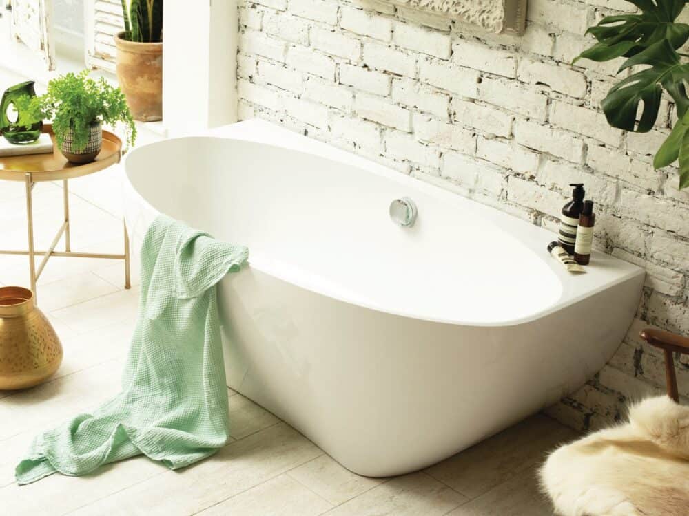 Waters Evolve back-to-wall bath against white-painted brick with a green towel and plants