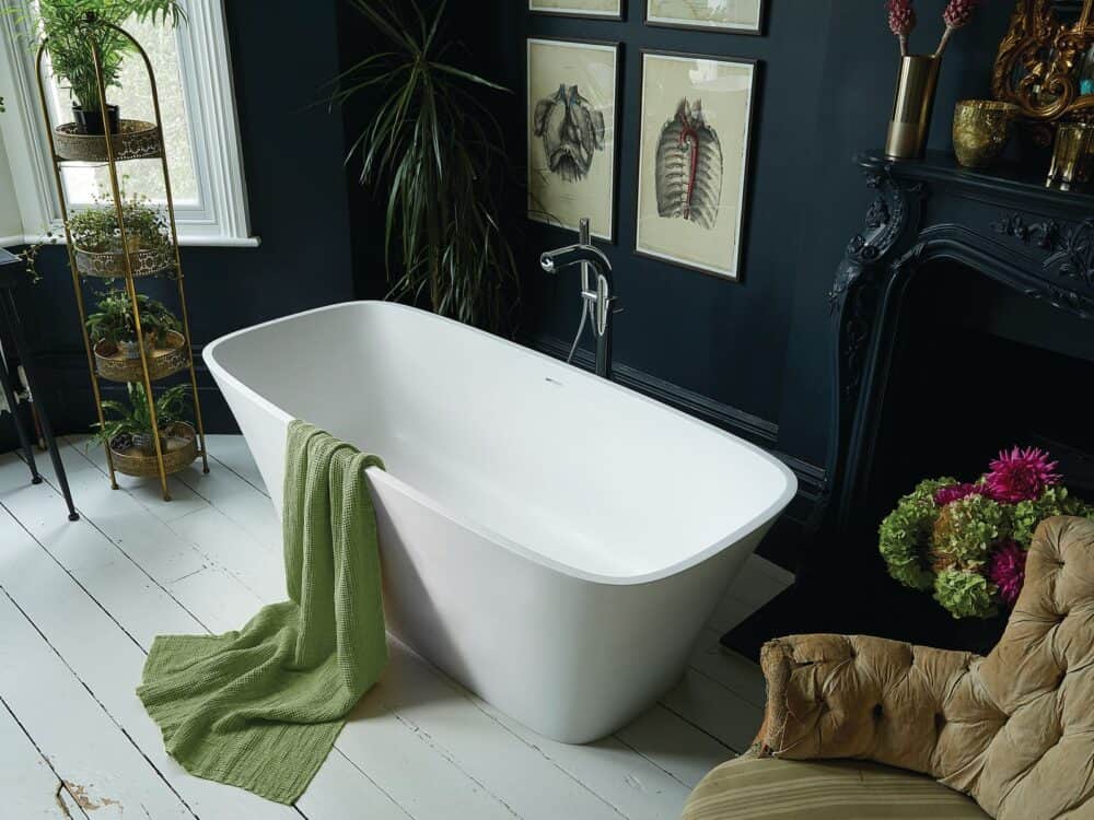 Waters Haze freestanding bath in a dark room with a fireplace, plants and a green towel