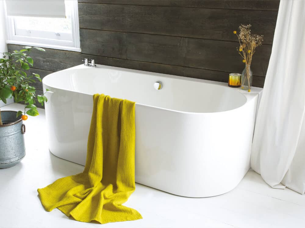 Waters Strait back-to-wall bath against a dark timber-clad wall with a yellow towel