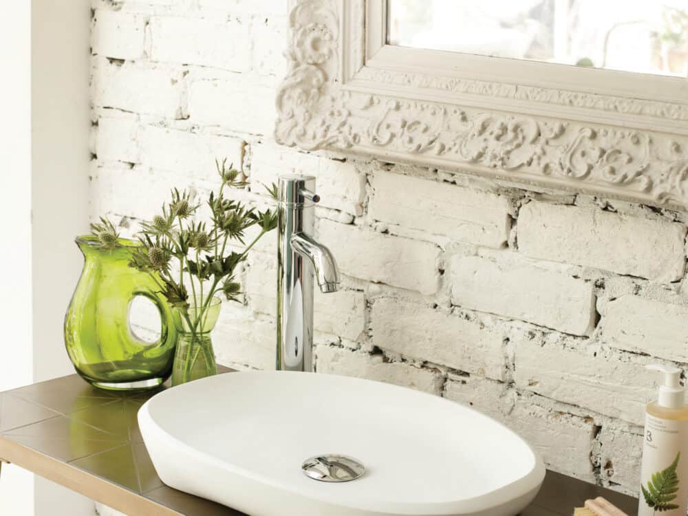 Waters Evolve counter basin on a timber top with a green glass vase against ornate white brick