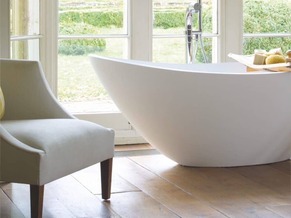 Waters Breeze freestanding bath beside a garden window with a pale armchair