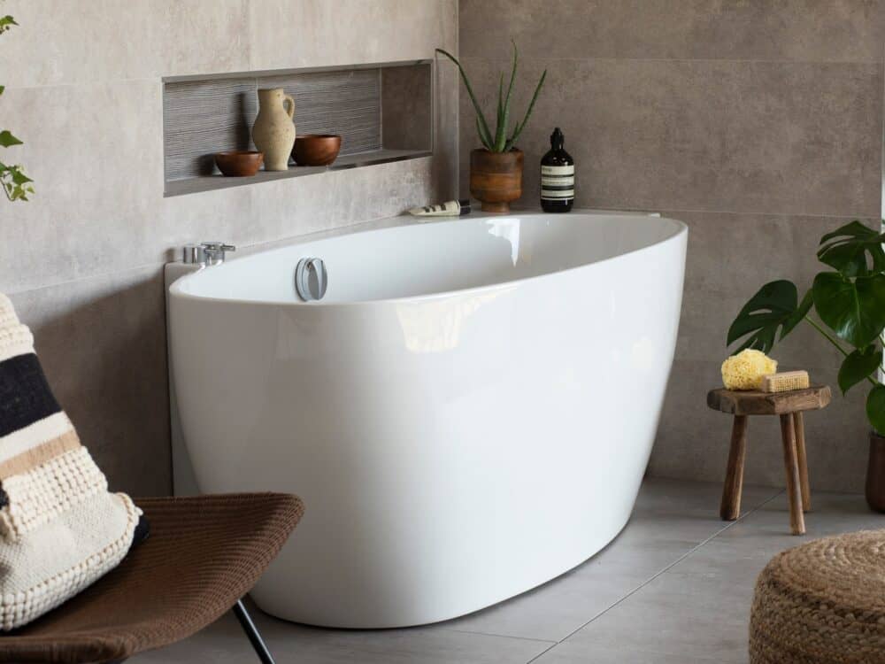 Waters Coast freestanding bath beside a tiled alcove with a timber stool and plants