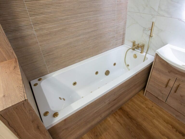 Whirlpool bath with brushed brass jets and a wood-effect bath panel in our Swansea showroom